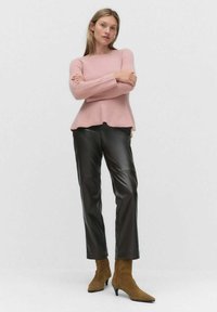 Pull en côtes rose avec un ourlet évasé, associé à un pantalon en cuir noir ajusté et des bottines en daim brun à bout pointu.