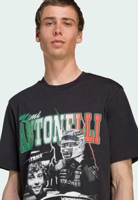 Black t-shirt made of cotton with a crew neckline, featuring colorful graphic prints of racing figures and bold text, "Kimi Antonelli."