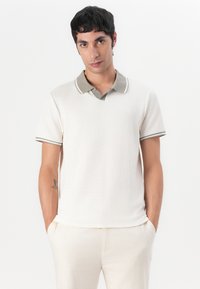 Baumwoll-Polohemd in Off-White mit strukturierter Oberfläche, kontrastierender beiger Kragen und Manschetten mit feinen Streifen. Taillierte Passform.