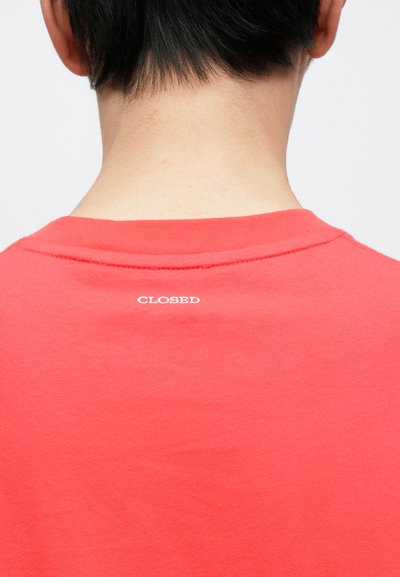Κόκκινο βαμβακερό t-shirt με στρογγυλή λαιμόκοψη, με μικρό λευκό κείμενο "CLOSED" στην πλάτη κοντά στον γιακά. Λείο ύφασμα.