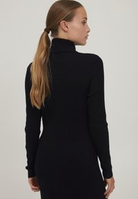 Abito nero a collo alto ribbed con maniche lunghe e silhouette aderente, realizzato in un tessuto liscio e con taglio a lunghezza media.