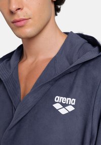 Pánský námořnický koupací plášť z měkké tkaniny, s žebrovaným límcem a bílým logem "arena". Nabízí hladkou texturu a uvolněný střih.