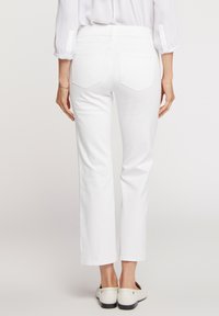 Jeans de mezclilla blanca con un diseño de pierna recta, acompañados de dos bolsillos traseros con solapas en forma de diamante. Combinados con zapatos claros.
