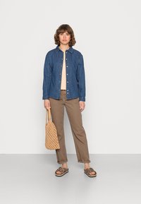 Camisa de ganga, blusa bege, calças castanhas e sandálias de estampado de leopardo, combinadas com uma bolsa de palha de cor creme. Design simples e texturas naturais.