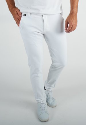 Pantalon slim blanc en tissu doux avec une texture lisse. Équipé d'une fermeture éclair à l'avant et d'un bouton, porté avec des baskets bleu clair.