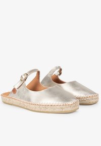 Zuecos de cuero metálico plateado con correa y hebilla en el tobillo, con detalles de yute alrededor de la suela y una textura lisa y brillante.