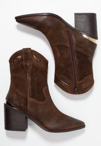 Hnědé semišové kotníkové boty s špičatou špičkou, blokovým podpatkem a zlatým zdobením na podpatku. Disponují bočním zipem a dekorativními výřezy.