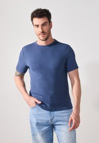 Blå, ribbestrikket t-skjorte med kort erm og rund hals, kombinert med lyseblå jeans. Stoffet har en teksturert overflate.