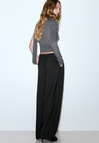 Szary top z długim rękawem o skróconym kroju w połączeniu z czarnymi, szerokimi spodniami z wysokim stanem. Gładki materiał, minimalistyczny styl.