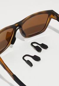 Gafas de sol de carey con lentes marrones, que cuentan con empuñaduras texturizadas negras. Incluye dos empuñaduras de goma negra adicionales.