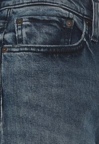 Mörkblå denimjeans med en klassisk femficksdesign, synliga sömmar och metallnitar vid ficköppningarna.