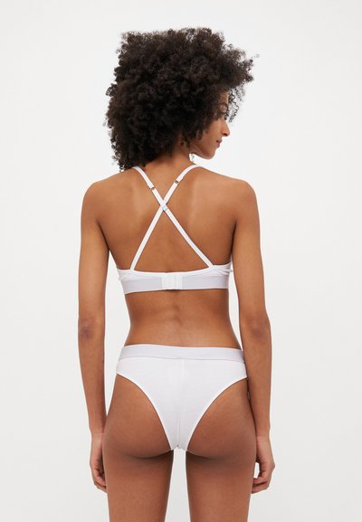 White lingerie set featuring a cross-back bralette with adjustable straps and matching thong. Smooth texture, minimal design, and elastic band.