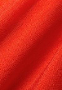 Tessuto rosso con una consistenza liscia e uniforme. Il materiale appare leggero ed è mostrato in una posizione drappeggiata, evidenziando il suo colore vivace.