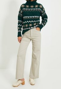 Vihreä neulottu villapaita, jossa on kukka- ja siksak-kuvioita, yhdistettynä vaaleanbeigeihin leveälahkeisiin housuihin ja valkoisiin puukengiltä, joissa on puu-urat.