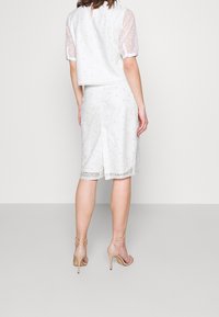 Ensemble blanc à deux pièces comprenant un haut à manches courtes avec une superposition texturée et une jupe longueur genou avec un léger éclat et une fente au dos.