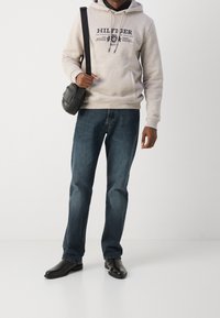 Sudadera con capucha de algodón gris claro con estampado negro "HILFIGER". Combinada con jeans de mezclilla azul oscuro y botas de cuero negras. Bolso cruzado negro.