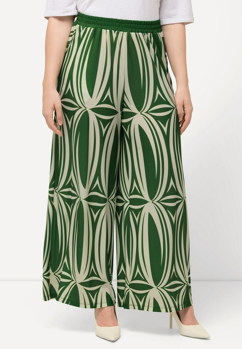 Grüne und beige weite Hosen mit einem auffälligen abstrakten Muster, elastischem Bund und leichtem Stoff. Kombiniert mit spitzen Schuhen.