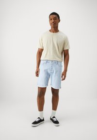 T-shirt beige chiaro, shorts in denim blu chiaro con orli arrotolati, calze grigie e sneakers nere. Design semplice senza pattern visibili.