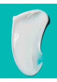 Gladde witte crème uitgespreid in een gebogen vorm op een effen turquoise achtergrond.