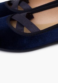 Tmavě modré sametové baleríny s kříženými saténovými pásky, kulatou špičkou a texturovaným podpatkem. Hladká vnitřní podšívka, flexibilní podrážka.