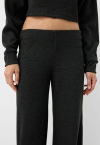 Mørkegrå ribbestrikket sæt bestående af top og bukser. Toppen er cropped med lange ærmer; bukserne har bred ben og høj talje.