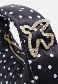 Torba z tkaniny w kropki w kolorze granatowym z białymi kropkami, z metalowymi detalami w kolorze złotym ozdobionymi biżuterią na uchwycie oraz zamknięciem na suwak.