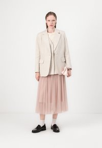 Beige linjakke over en kremfarget topp, med en lys rosa tyllskjørt. Svarte loafers og en liten rosa veske fullfører antrekket.