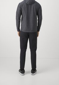 Veste à capuche grise, pantalon noir, coupe athlétique. La veste a une texture lisse, le pantalon est élégant avec des poches, associé à des chaussures de course noires.