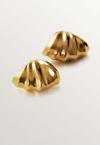 Pendientes dorados con un diseño de borde ondulado, que presentan estrías y un acabado brillante. Cada pendiente tiene una forma redondeada y con ondas.