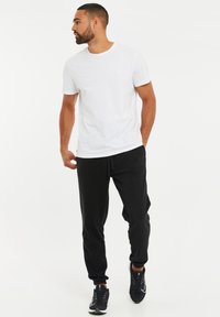 Witte katoenen t-shirt met ronde hals; gecombineerd met zwarte joggingsbroeken met elastische boorden. Schoenen zijn zwart met witte accenten.