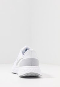 Chaussure de sport blanche avec des accents gris et une semelle texturée. Comprend un talon rembourré et une tige en mesh cousue pour la respirabilité.