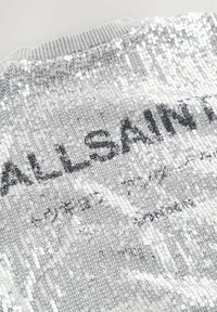 Srebrny sweter z cekinami, z prążkowanym dekoltem i nadrukowanym tekstem "ALLSAINTS". Posiada fakturowaną powierzchnię i odbijające światło cekiny.