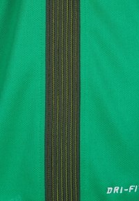 Tissu de sport vert avec une bande verticale noire et des coutures jaunes, étiqueté "DRI-FIT" dans le coin inférieur droit.