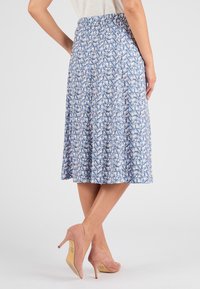 Jupe à motifs bleus avec une taille cintrée, tissu fluide et motifs géométriques en blanc, rose et marine. Portée avec des escarpins roses.
