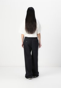 Pantalons larges noirs au fit décontracté, avec une taille élastique et deux poches arrière. Associés à un haut blanc ample, vus de dos.
