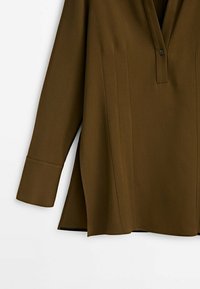 Chemise marron à manches longues avec un col en V, dotée d'un détail de bouton et de plis subtils ; texture lisse et coupe décontractée, légèrement allongée.