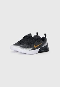 Sapatos atléticos em preto e branco com um padrão de bolinhas, apresentando um logo da Nike em dourado, atacadores pretos e uma sola branca com uma unidade de ar visível.