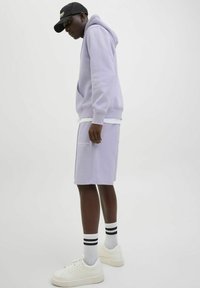 Ljuslila hoodie och matchande shorts av mjukt tyg. Vita sneakers med tjocka sulor och svartspräckta strumpor. Enkel design, inga mönster.