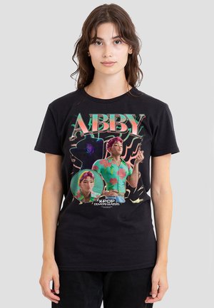 Young woman wearing black T-shirt with colorful graphic of animated character "Abby" from K-pop Demon Hunters series.