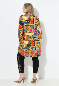 Camisa larga colorida con estampado floral y animal, combinada con leggings negros con bordado dorado y tacones decorados.