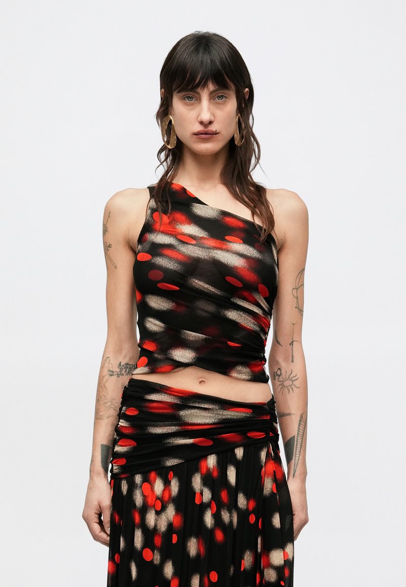 Μαύρο τοπ με ασύμμετρο σχέδιο, διακοσμημένο με κόκκινα και χρυσά κυκλικά μοτίβα. Το ύφασμα είναι λείο και εφαρμοστό, συνδυασμένο με φούστα που ταιριάζει.