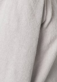 Světle šedá, měkká vlna látky svetr s jemnou žebrovanou strukturou a splývavým designem, ukazující záhyby a sklady pro uvolněný vzhled.