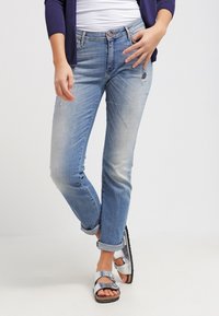 Vaaleansiniset farkut, joissa on rento malli, hienovaraisia haalistumia ja repeämiä, yhdistettynä hopeisiin sandaaleihin ja laivastonsiniseen neuletakkiin.