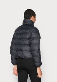 Giubbotto nero imbottito con colletto alto, design trapuntato e polsini elastici. Caratterizzato da una texture lucida e liscia e da un taglio corto.