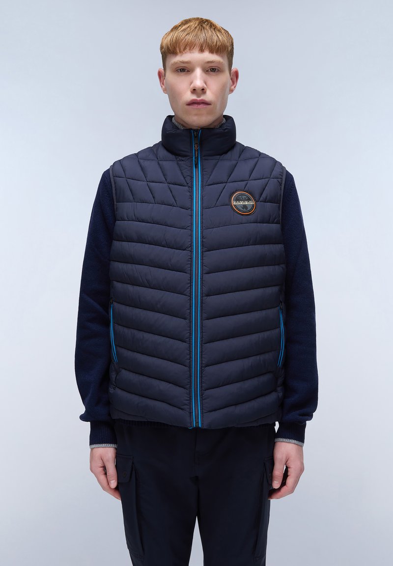 Marinblå pufferväst med en vadderad design och blå dragkedja. Har en hög krage och en logopatch på bröstet.