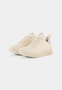 Sneaker beige con una parte superiore liscia in materiale sintetico, design con lacci e suola spessa e rigata. Presenta un accento argento sul tallone.