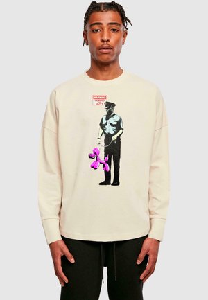 Cream oversized sweatshirt featuring a graphic of a figure with a pink balloon dog and a “WARNING GUARD DUTY” label. Soft texture.
