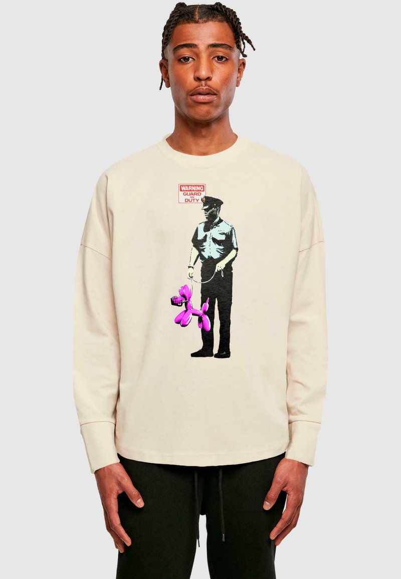 Cremfarbener Oversized-Sweatshirt mit einer Grafik einer Figur, die einen pinkfarbenen Luftballonhund und ein "ACHTUNG WACHDIENST"-Schild zeigt. Weiche Textur.