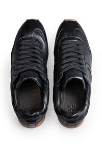 Para czarnych skórzanych sneakersów z czarnymi sznurowadłami i brązowymi podeszwami widziana z góry na białym tle.