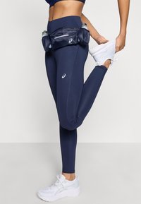 Μαρίνα μπλε κολάν με εφαρμοστό σχέδιο, που διαθέτουν πλαϊνές λεπτομέρειες από δίχτυ και τσέπη στη μέση. Άσπρα αθλητικά παπούτσια ολοκληρώνουν την εμφάνιση.